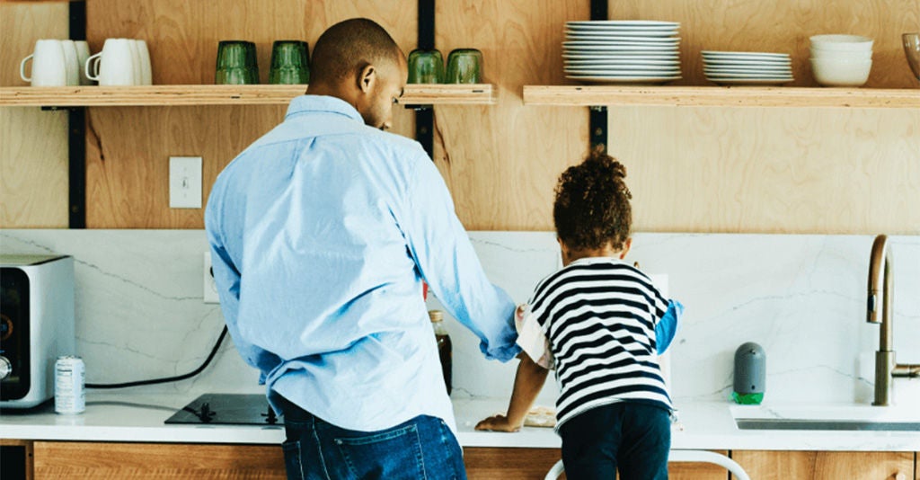Father and child happily doing house chores together in the kitchen.