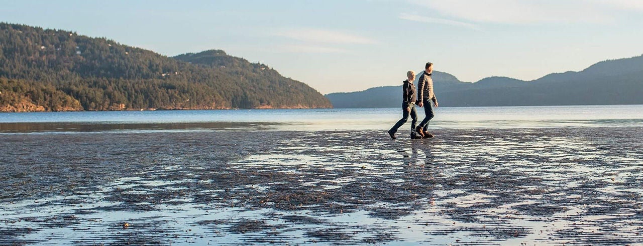 Australian couple walking along a beach at sunset with hills in the background. 