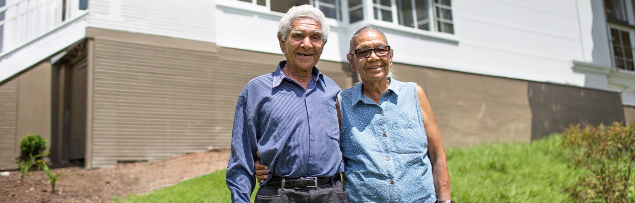 Proud seniors in front of Australian brick suburban home.