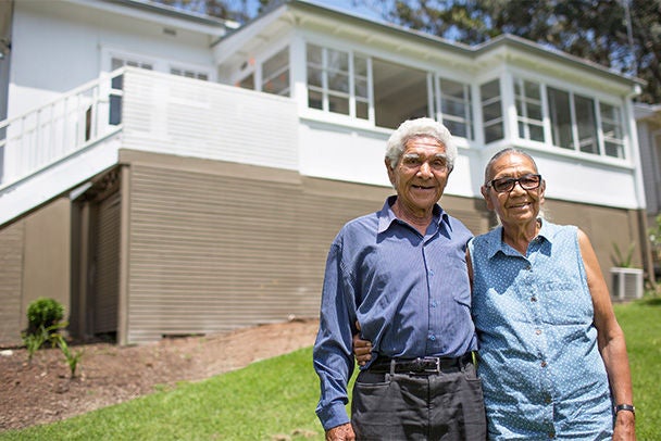 Proud seniors in front of Australian brick suburban home.