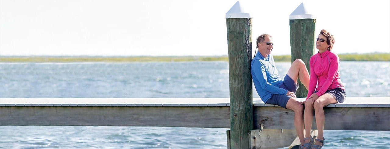 Happy couple sitting on a bridge with the sea in the distance, relaxing together.