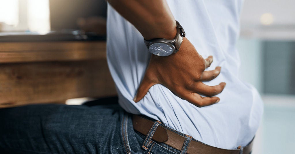 Person experiencing lower back pain while working at a desk.