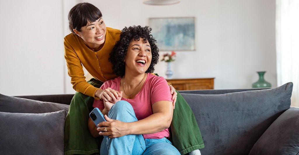 Cheerful diverse lesbian couple in living room smiling.