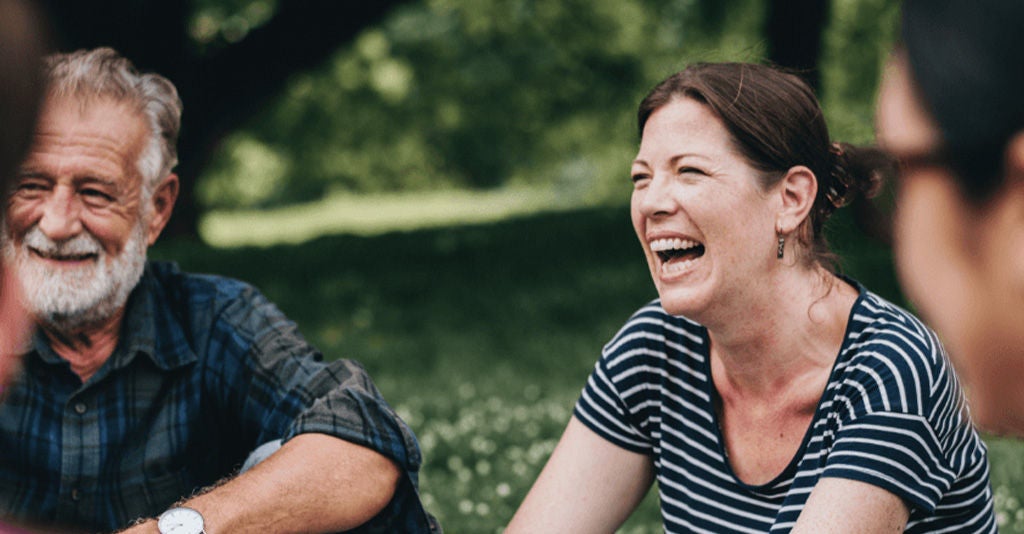 Supportive group of people sitting on the grass in a park smiling.