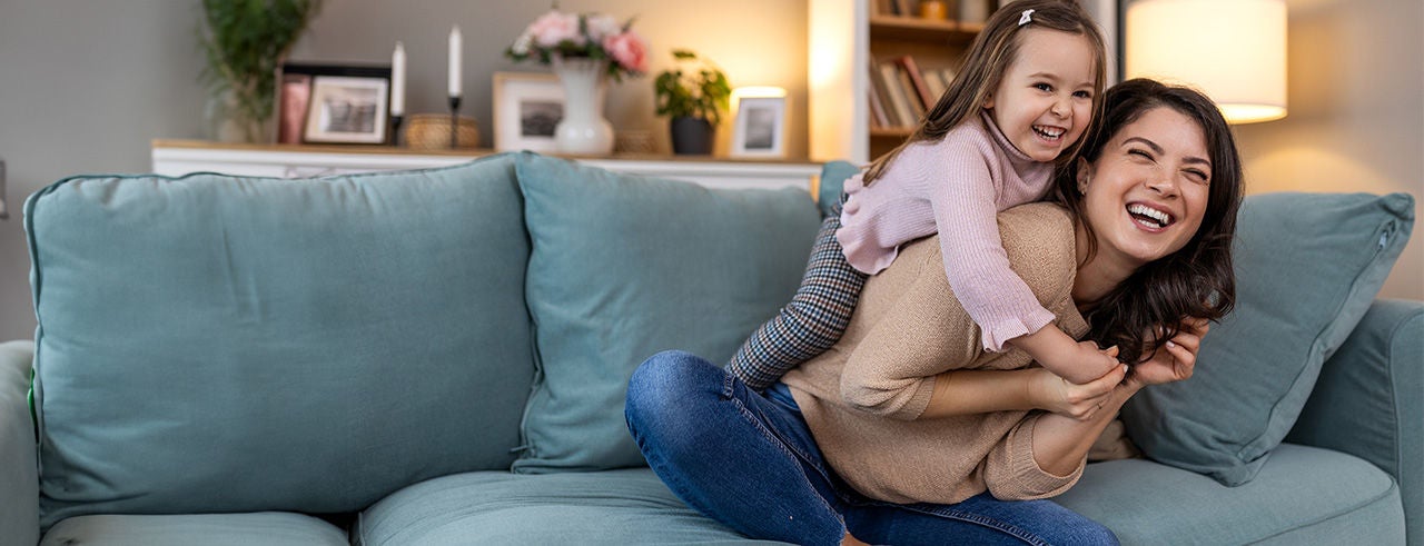 A little girl hugging her smiling mother while she is holding her on the home living room sofa.