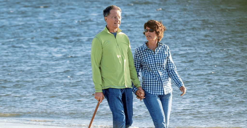Man with a cane walking with his wife on the beach.