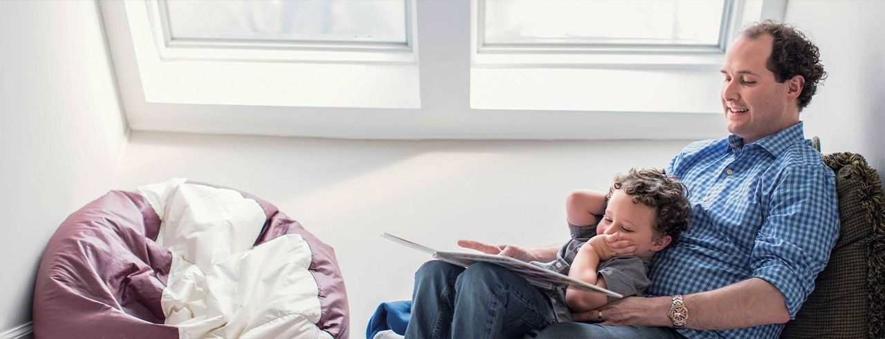 Father help son in studying while seating on sofa.