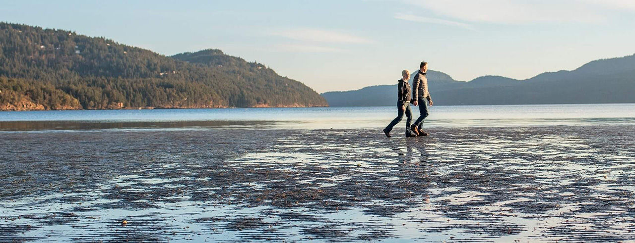 Couple walking on beach while holding hands of each other.